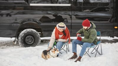 Young couple travelling in winter with trailer van and cute dog